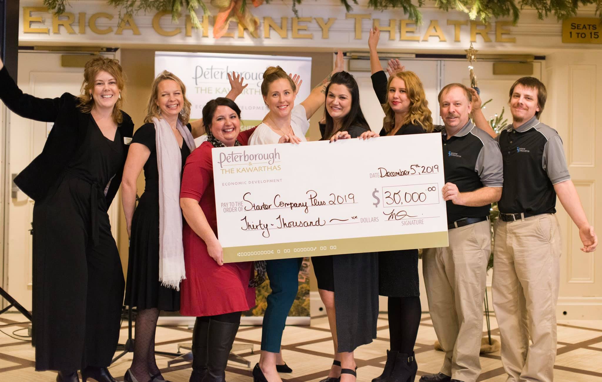 eight happy people holding a cheque and one hand in air