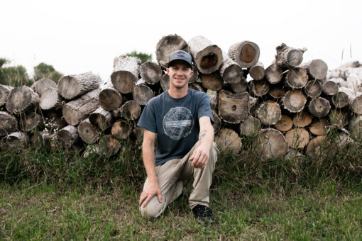 a man kneeling on one knee with a bunch of logs in the background