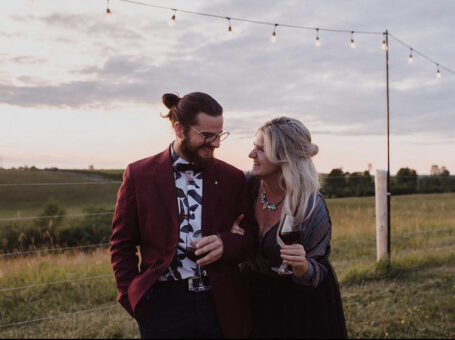 a man and woman at a farm wedding laughing and having wine