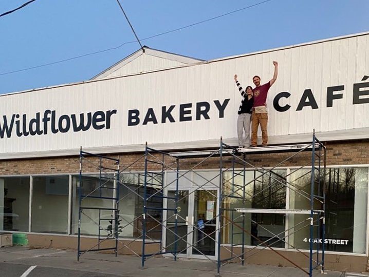 man and woman on ladder work platform with signboard behind reading "wildflower bakery cafe"