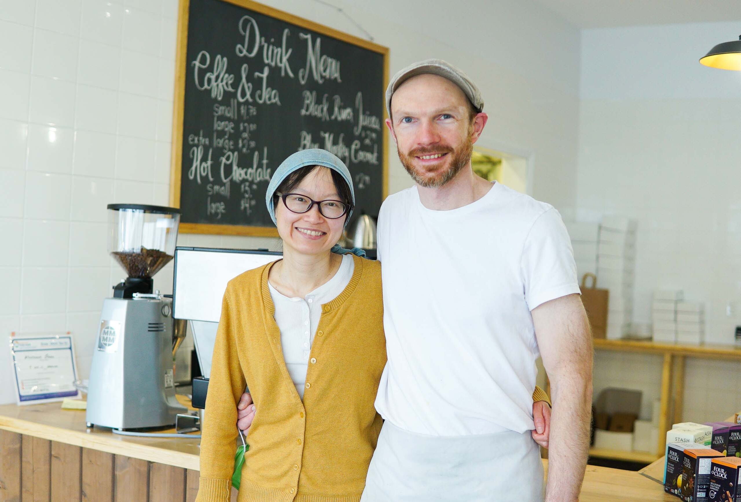 a man and woman in front of bakery counter with chalkboard menu behind them
