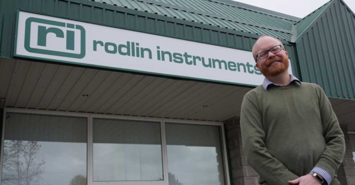 A person stands in front of a building with a sign reading "Rodlin Instruments"
