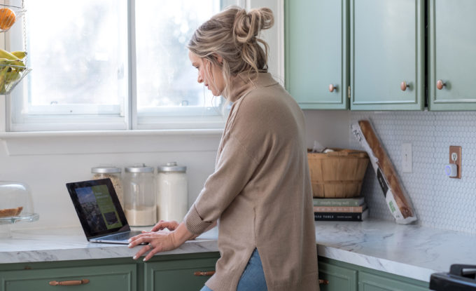 A woman using a laptop while standing at her kitchen counter
