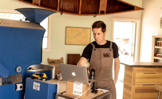 A man wearing an apron working on a laptop next to machinery