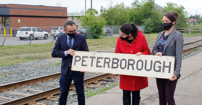 Three people hold a sign that reads "PETERBOROUGH"