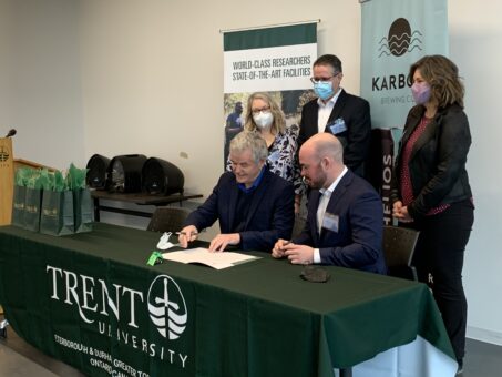 image of people signing a document with Trent University and Karbon Brewing Co banners in the background