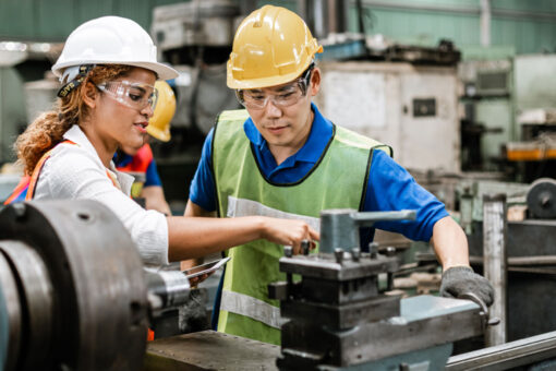 two people stand over a piece of manufacturing machinery