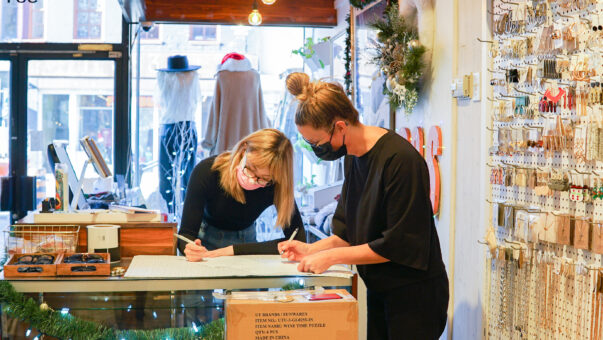 two women facing each other writing down information on paper at the front counter of a small business