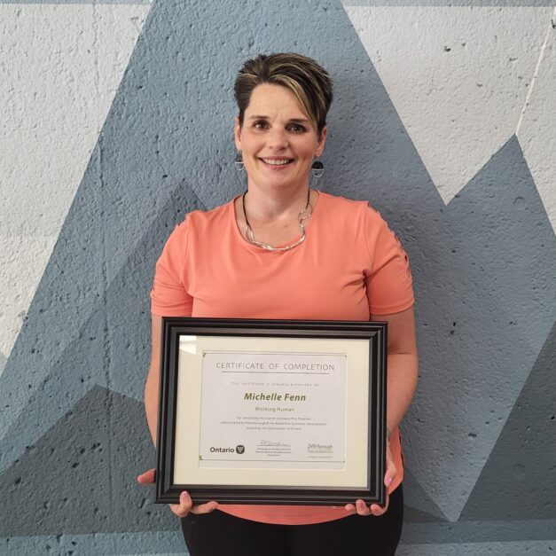 Michelle Fenn standing in front of a geometric background holding a Starter Company Plus certificate