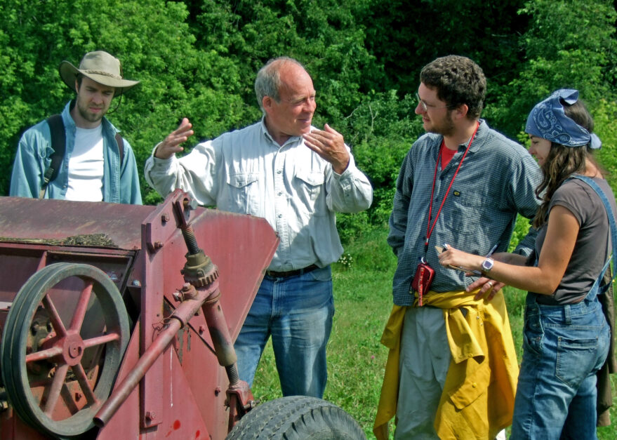 David Cohlmeyer speaks to two men and a woman with a piece of farm equipment in front of them.