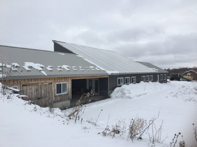 a passive solar green house on a farm during the winter with snow around it
