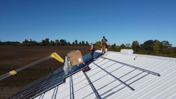 Two people on top of a barn roof installing solar panels