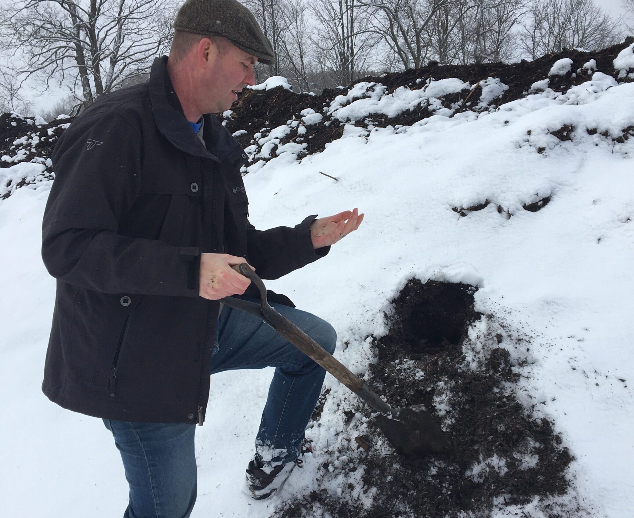 Man in coat and jeans placing a shovel into the ground