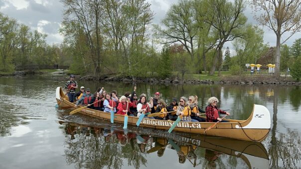 Group of travel media paddling in a large voyager canoe on the waterway in Peterborough, Ontario