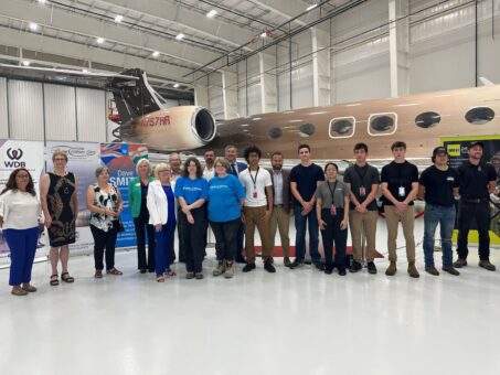 A group of people standing in a line for a phone in front of an airplane in a hanger